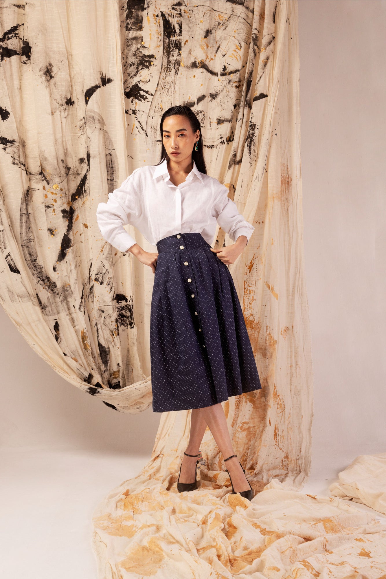 A-line skirt in blue polka dot sateen with pearl buttons, front pleats, and side pockets; artisan-made luxury womenswear from India