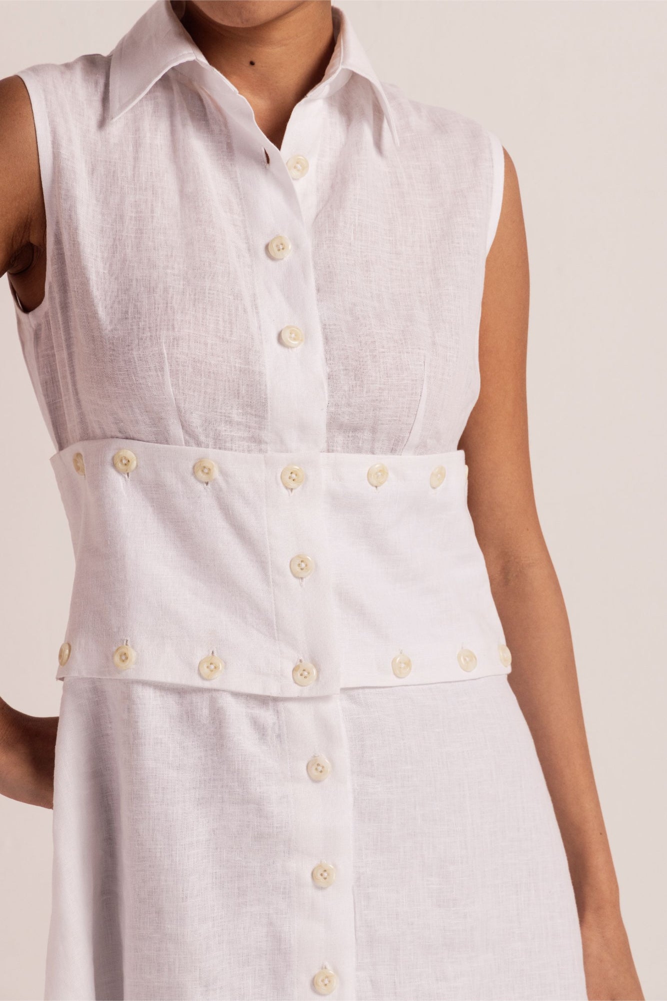 Sleeveless white linen dress with classic collar, front button opening, and detachable section for versatile styling; artisan-crafted luxury