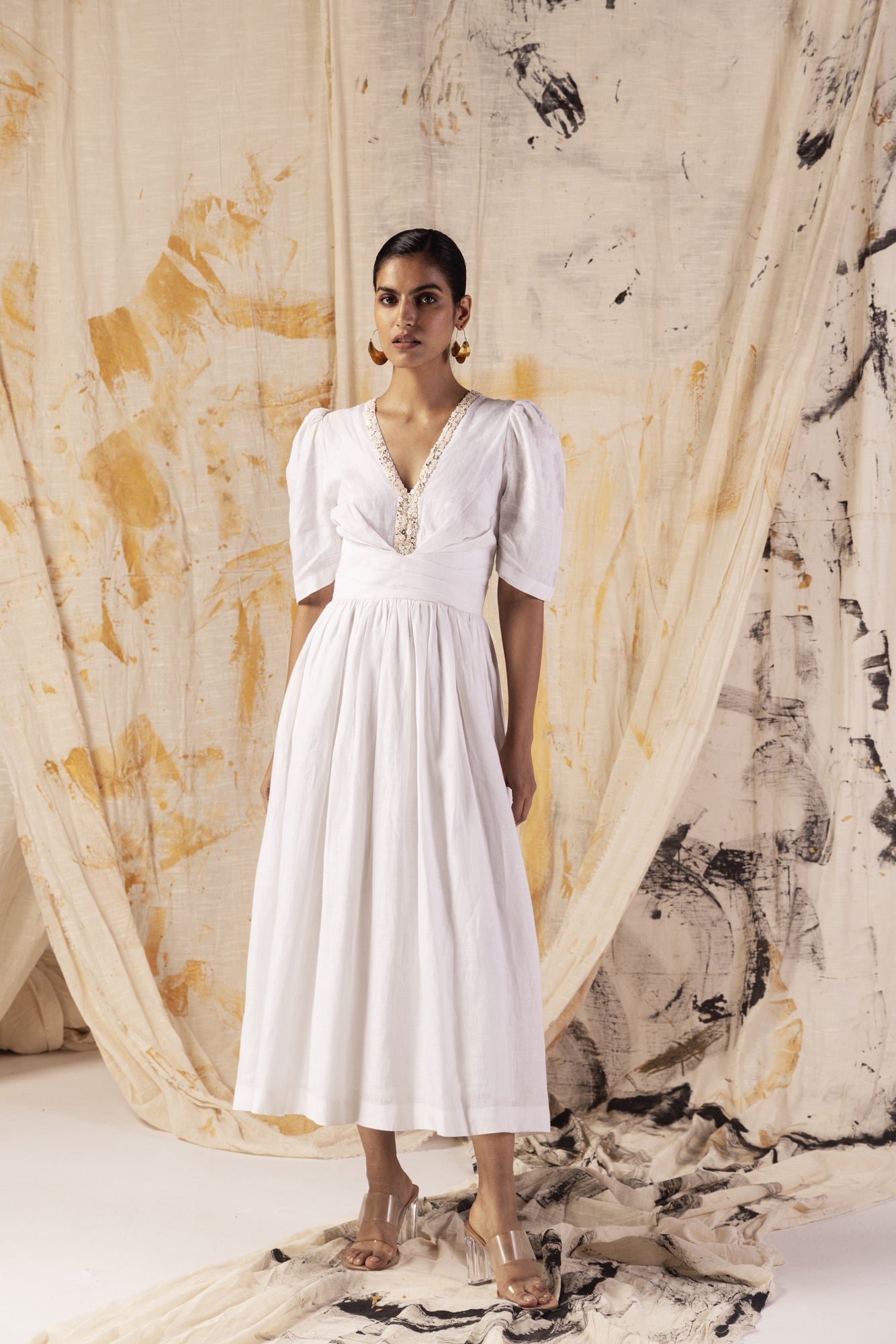Elegant white linen dress with V-neck, repurposed button details, sculpted waist with pleats, and subtle shoulder puffs, exuding luxury