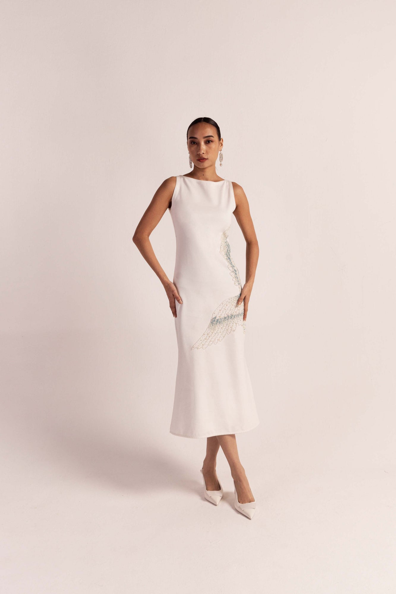 White mermaid-style dress with ribbed round neckline, sleeveless design, and hand-embroidered crane in shell pearls, exuding luxury and artistry
